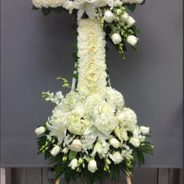 White floral cross on an easel with lilies and roses