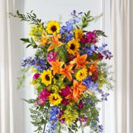 Tall standing floral spray with sunflowers, lilies, and blue flowers