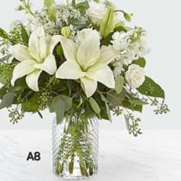 White lilies and mixed white flowers in a clear glass vase