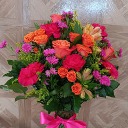 Tall vase arrangement of bright orange roses and hot pink flowers with a pink bow.