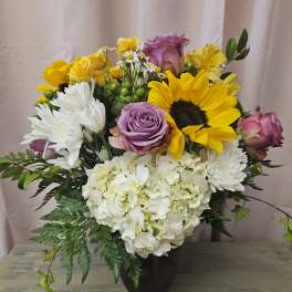 Bouquet of sunflowers, roses, daisies, and white hydrangeas in a dark vase