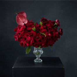 Red rose arrangement in a clear glass vase with a pink anthurium accent