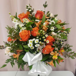 Orange roses and white daisies in a clear vase with a white ribbon