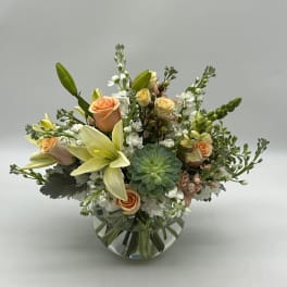 Peach roses and pale lilies in a round glass vase