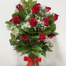 Red roses arranged in a clear glass vase with baby's breath and a red ribbon