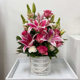 Pink lilies and roses arranged in a white basket with pearl trim