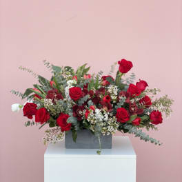 Red roses arranged in a gray rectangular vase with white filler flowers