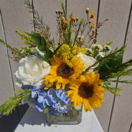 Bouquet of sunflowers, white roses, and blue hydrangea in a glass vase