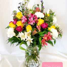 Mixed bouquet of pink, yellow, and white flowers in a glass vase