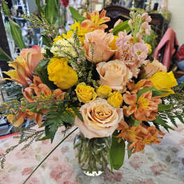Mixed bouquet of peach and yellow roses with orange alstroemeria in a glass vase