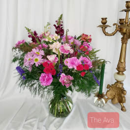 Pink and purple mixed bouquet in a glass vase beside a gold candlestick
