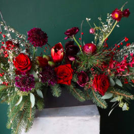 Red roses and burgundy flowers in a low arrangement with pine branches