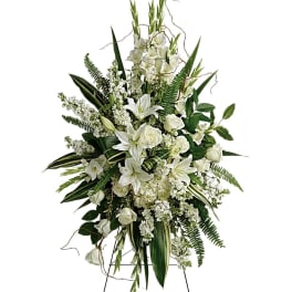White funeral spray with lilies, roses, and greenery on an easel