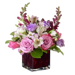 Pink and lavender flowers arranged in a red glass vase