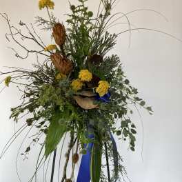 Tall wildflower arrangement with yellow blooms and dried seed pods on a stand