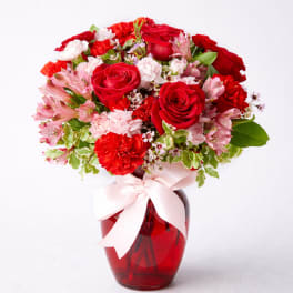 Red roses and pink carnations in a red glass vase with a pink ribbon