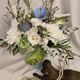 White and blue floral arrangement in a light blue vase with a shell accent