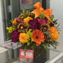 Colorful mixed flower arrangement in a basket with an orange bow
