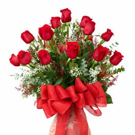 Red roses arranged in a pink patterned vase with a large red bow