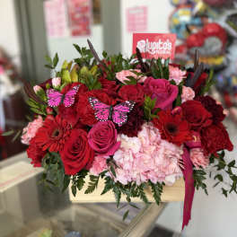 Red and pink rose bouquet with hydrangea and butterflies in a wooden box