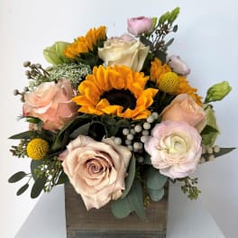 Mixed bouquet with sunflowers, roses, and pale pink blooms in a wooden box
