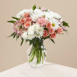 Pastel bouquet of white daisies, pink roses, and carnations in a clear glass vase