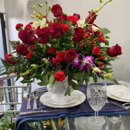 Red rose centerpiece in a clear glass vase on a set table