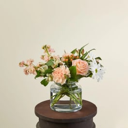 Low arrangement of peach roses and carnations with white daisies in a clear glass vase
