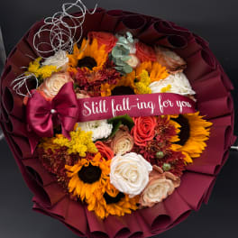 Bouquet of sunflowers and roses wrapped in burgundy paper with a ribbon