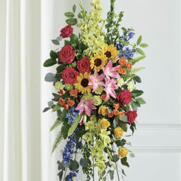 Tall floral standing spray with roses, lilies, sunflowers, and blue accents