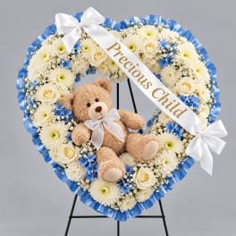 Heart-shaped floral wreath with a teddy bear and ribbon on a stand