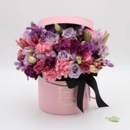 Pink hatbox arrangement with purple and pink flowers and a black ribbon