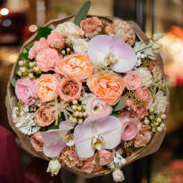 Bouquet of peach and pink flowers with pale orchids wrapped in brown paper