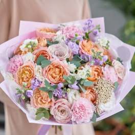 Pastel bouquet of roses, carnations, and purple flowers wrapped in pink paper