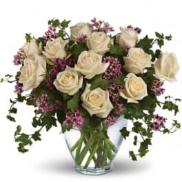 Cream roses and purple filler flowers in a clear glass vase