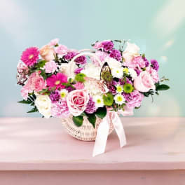 Pink and white mixed flower arrangement in a wicker basket with a ribbon