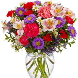 Mixed bouquet of pink, purple, and white flowers in a clear glass vase