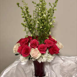 Tall bouquet of red, pink, and white roses in a burgundy vase