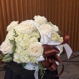 White rose and hydrangea bouquet in a basket with satin ribbons