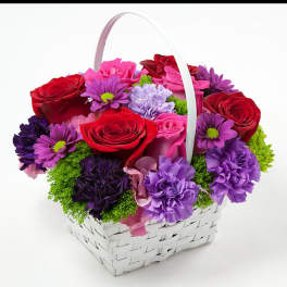 Basket of red, pink, and purple flowers with a white handle