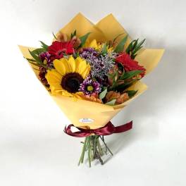 Mixed bouquet with a sunflower, red gerberas, and purple flowers in yellow wrap