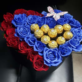 Heart-shaped arrangement of red and blue roses with gold-wrapped chocolates