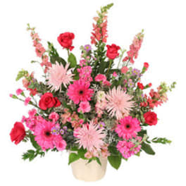Pink and red mixed flower arrangement in a cream vase