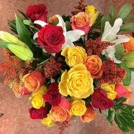 Top view of bright bouquet of red, yellow, and orange roses with white lilies