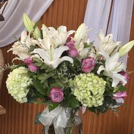 White lilies and pink roses in a glass vase with hydrangeas