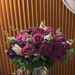 Purple roses and hydrangeas in a glass vase with ribbon