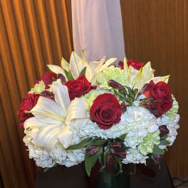 Bouquet of red roses, white lilies, and pale hydrangeas in a glass vase