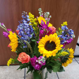 Colorful mixed bouquet with sunflowers, roses, and blue flowers in a glass vase