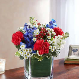 Colorful bouquet of red, blue, and white flowers in a square glass vase