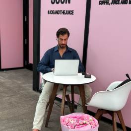 Large pink bouquet of roses in a pink gift bag beside a seated man with a laptop